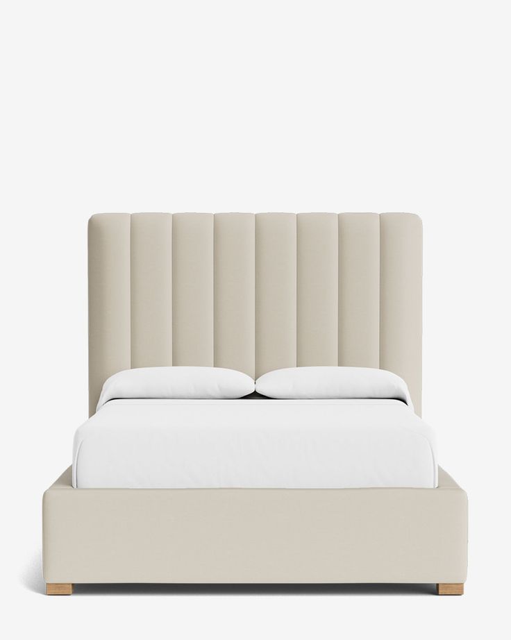 an upholstered bed with white sheets and pillows