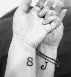 two people holding hands with tattoos on their wrists and one has the letter j on it