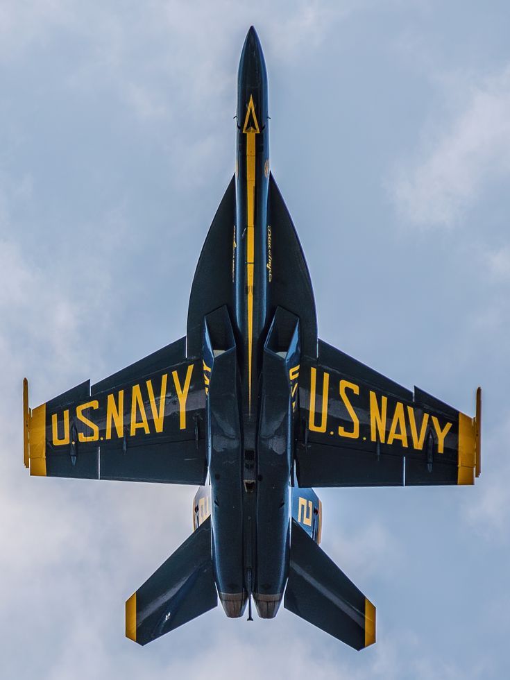 a navy jet flying in the sky with it's landing gear down