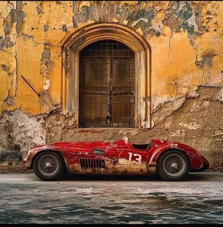 an old red sports car is parked in front of a yellow wall with peeling paint