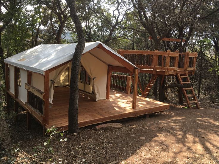 a small tent in the woods with a swing set and tree house on it's deck