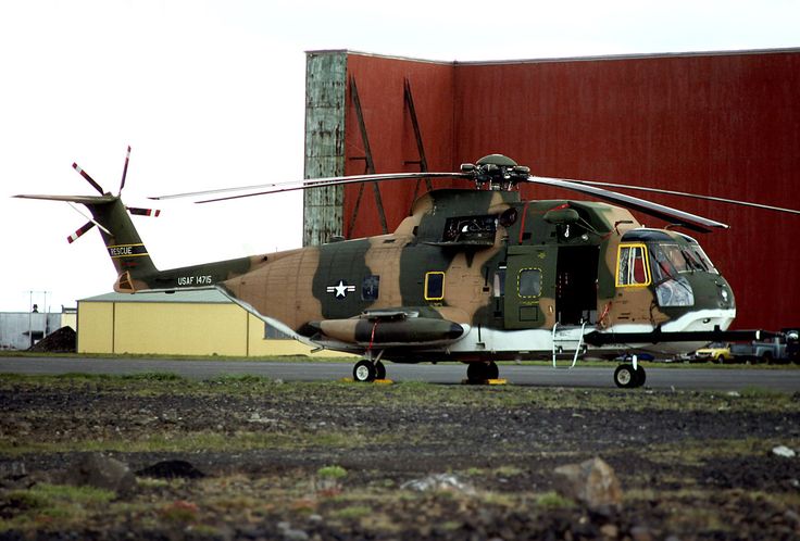 an army helicopter is parked on the tarmac near a building with a red wall