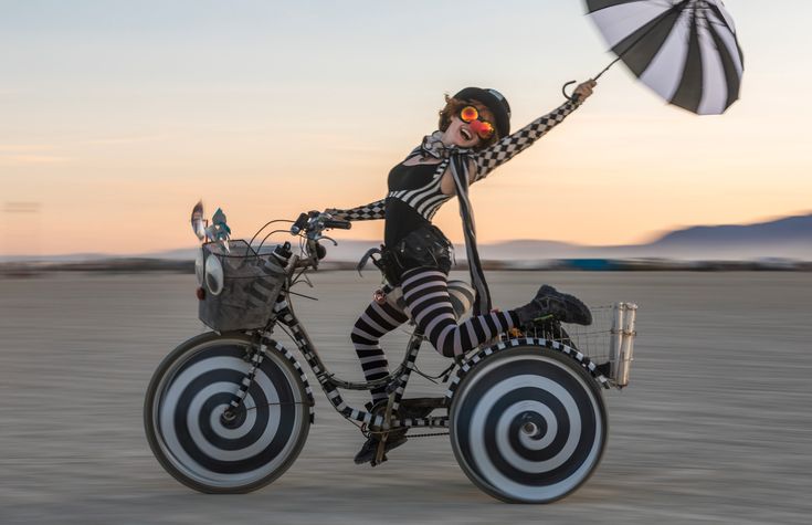 a woman dressed in black and white riding a bike with an umbrella on the back