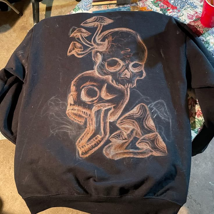 a black sweatshirt with a drawing of a skeleton and a skull on the back, sitting on a chair