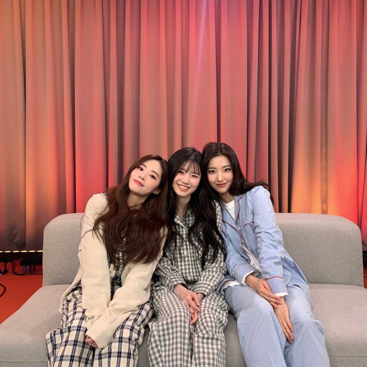 three young women sitting on a couch in front of a red and orange curtained background