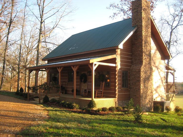 a log cabin sits in the middle of a grassy area with trees and shrubs around it