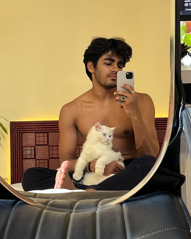 a man taking a selfie in front of a mirror with a cat on his lap