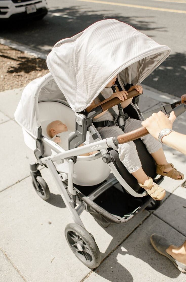 a woman pushing a stroller with a baby in it's seat on the sidewalk