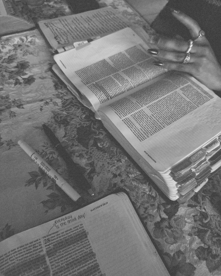 a person sitting at a table with several open books on top of it and writing