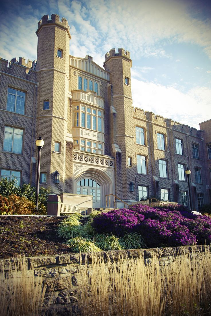 a large brick building with many windows and flowers in the foreground on a sunny day