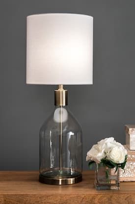 a glass table lamp sitting on top of a wooden table next to a vase with white flowers