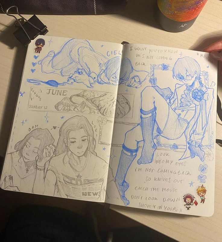 an open notebook with drawings on it sitting next to a can of soda and other items