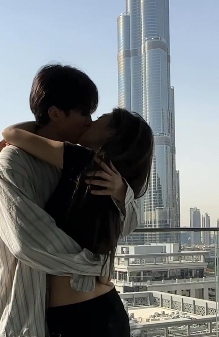 a man and woman kissing in front of a cityscape with skyscrapers behind them