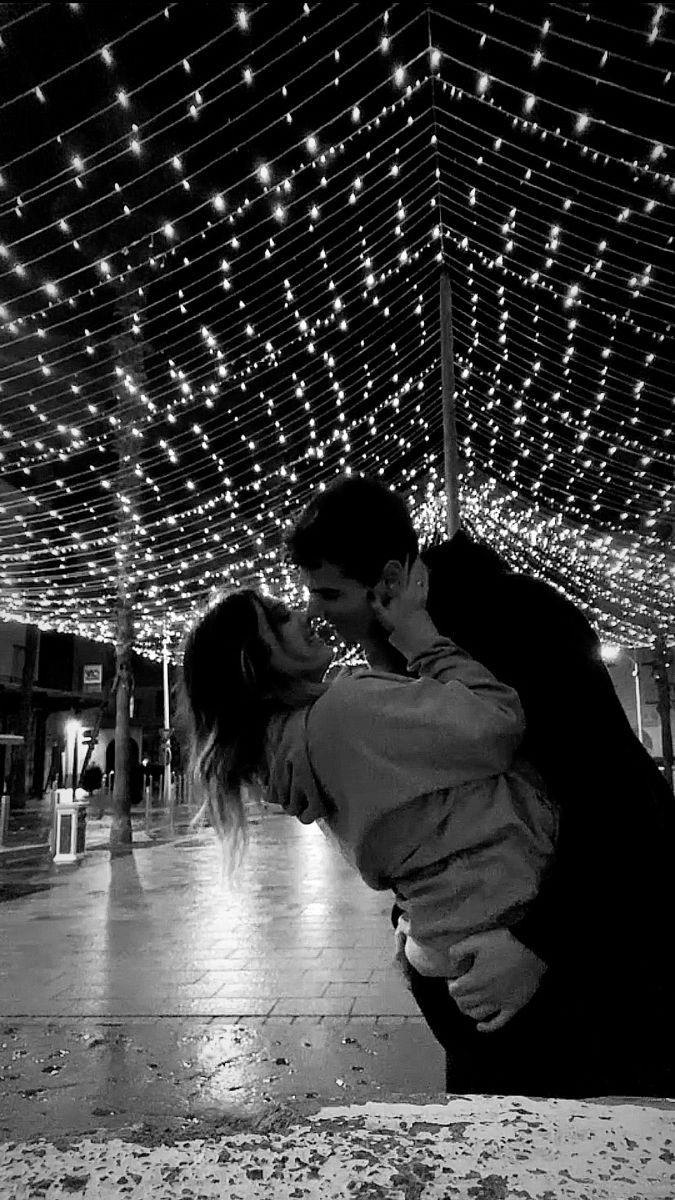 a man and woman kissing in front of string lights on the ceiling at night time