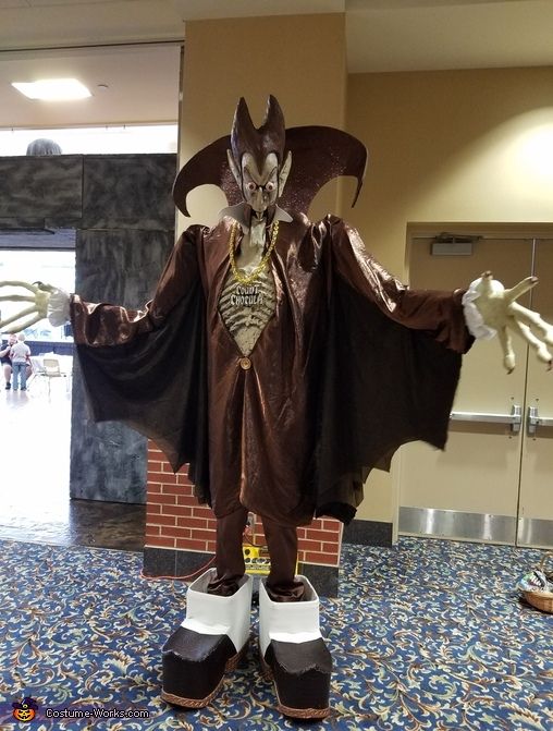 a man dressed up as a demon standing on top of a blue carpeted floor