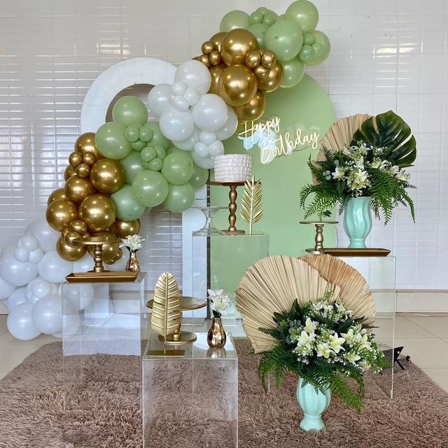 balloons and flowers are on display in front of a wall with gold, white and green decorations