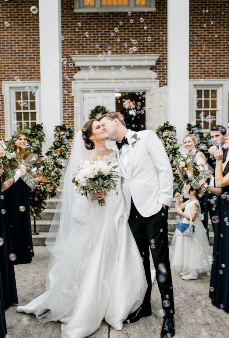 a newly married couple kissing in front of their wedding party with bubbles coming from them