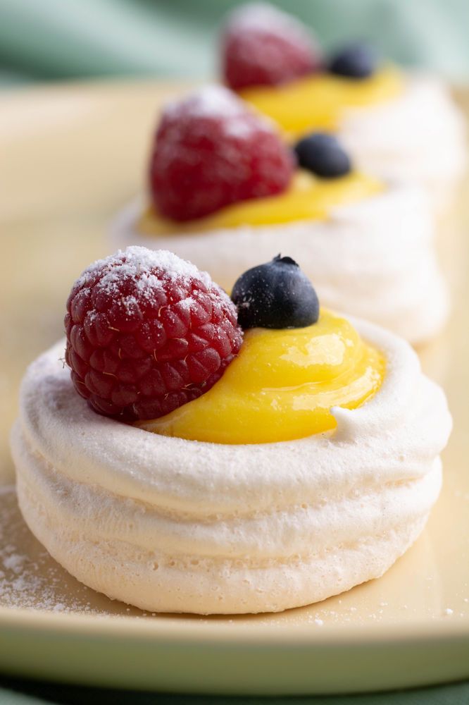 three desserts on a plate with raspberries, blueberries, and lemon