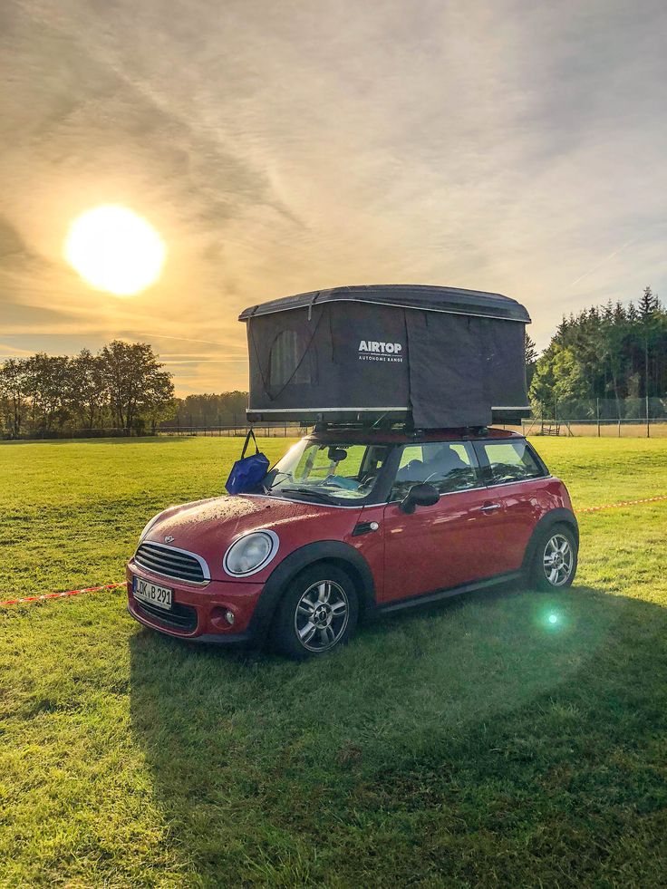 a small red car parked on top of a lush green field under a cloudy sky