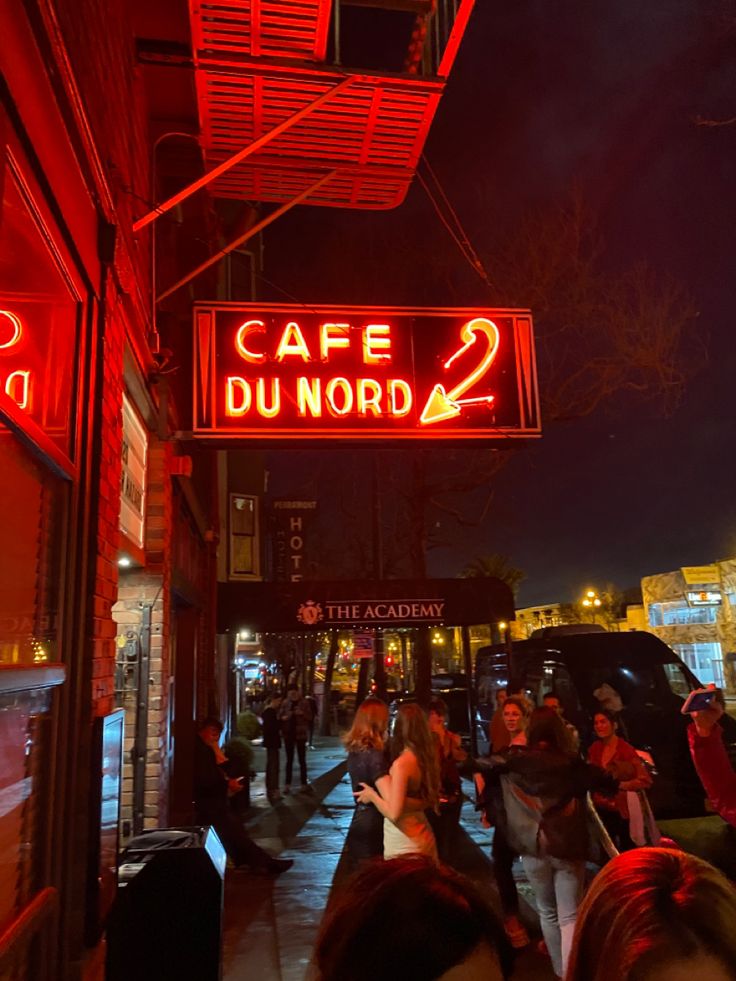 people are walking down the sidewalk in front of cafe du noord 2 at night