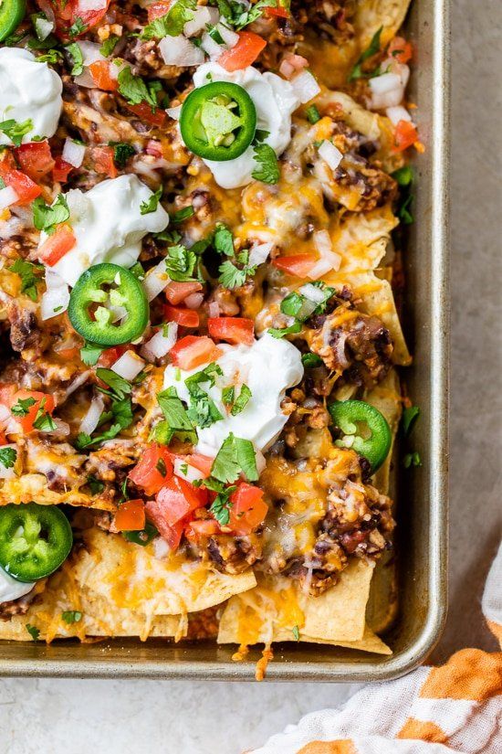 nachos in a baking dish with sour cream and green peppers