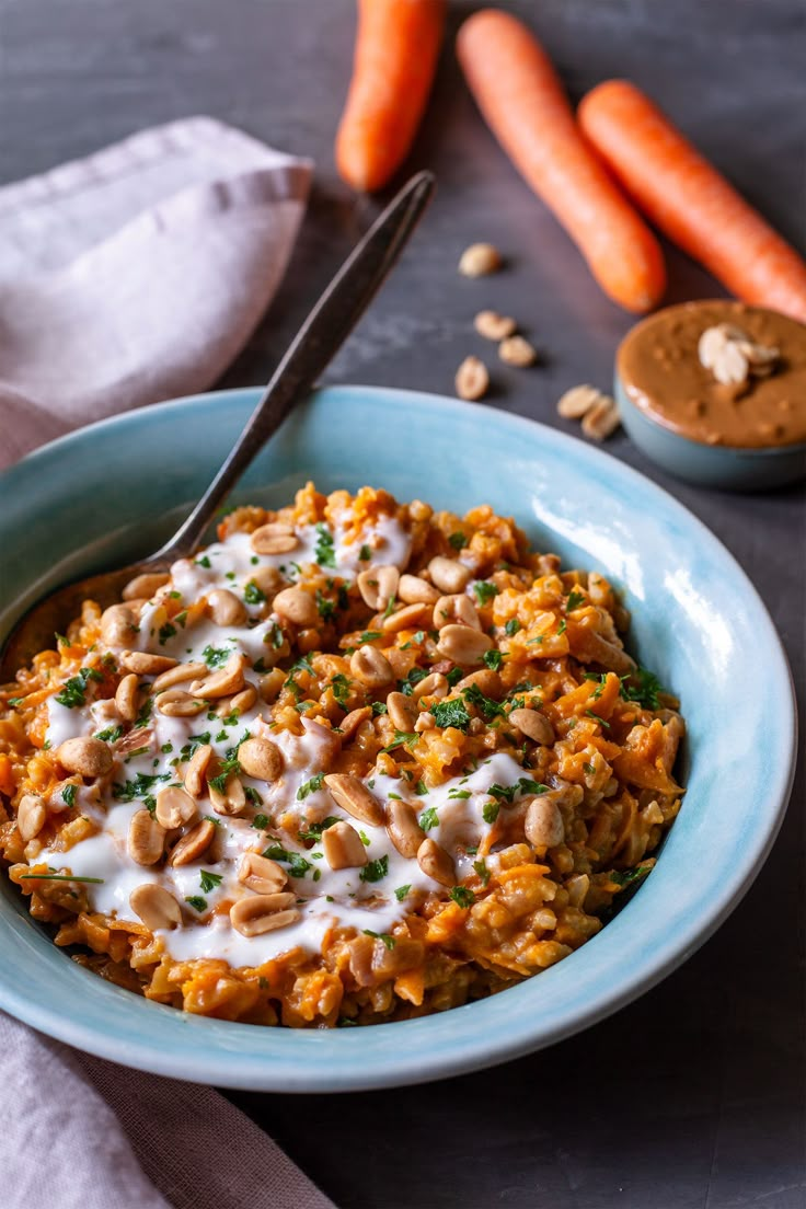 a bowl filled with carrots, rice and cashews on top of a table