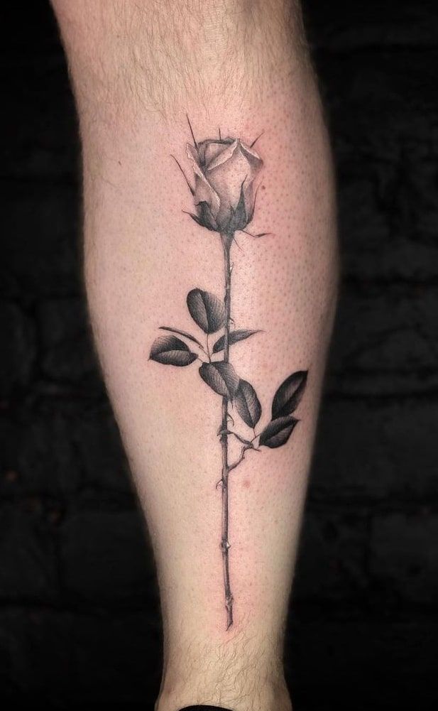 a black and white rose tattoo on the left leg, with leaves growing out of it