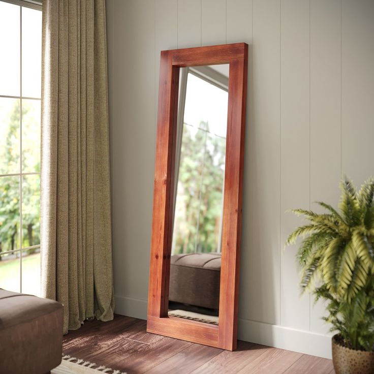 a large mirror sitting on top of a wooden floor next to a plant in a living room