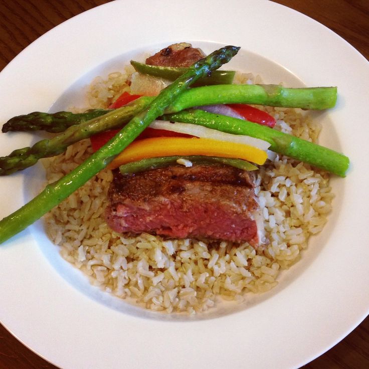 a white plate topped with rice and veggies next to meat on top of asparagus