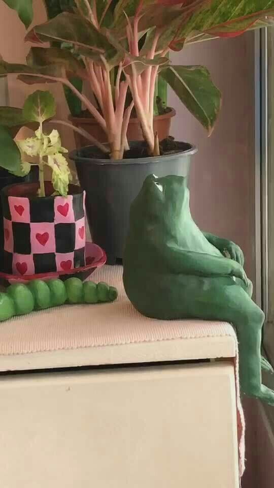 a green frog statue sitting on top of a table next to a potted plant