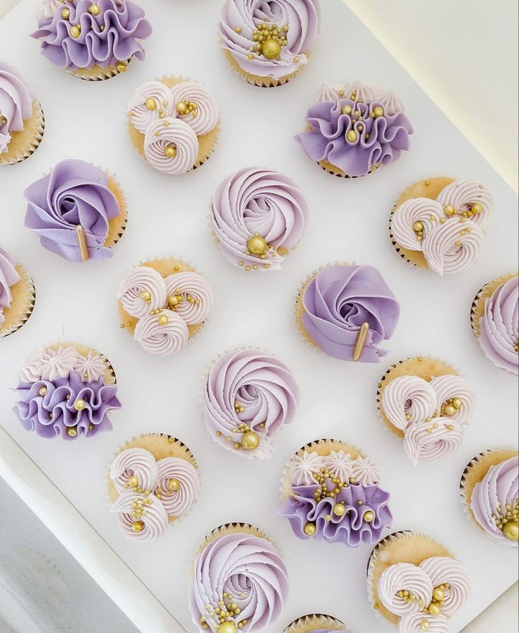 cupcakes with purple frosting and gold decorations are arranged on a white tray