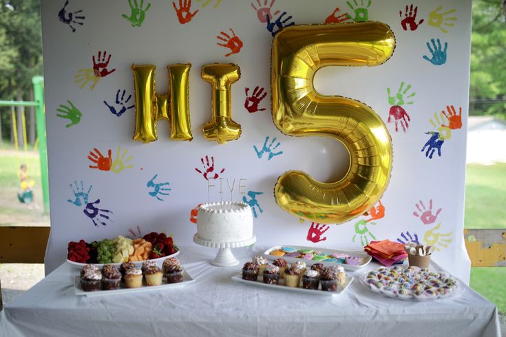 a table with cake, cupcakes and balloons that say five in gold letters