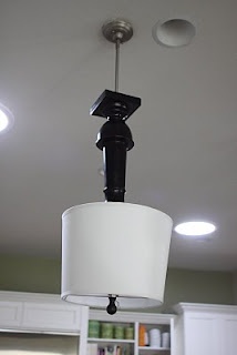 a light fixture hanging from the ceiling in a kitchen with white cabinets and cupboards