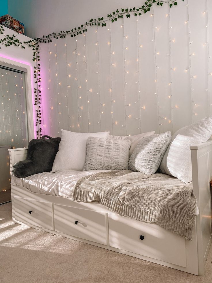 a white daybed with drawers underneath it in a room filled with lights and greenery