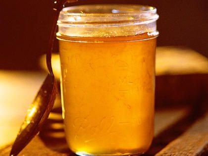 a jar filled with honey sitting on top of a wooden table next to a knife