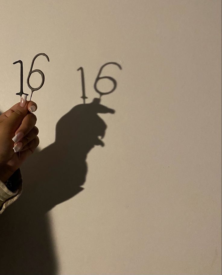 someone is writing numbers on the wall with their hands and shadow behind them that reads'16 '