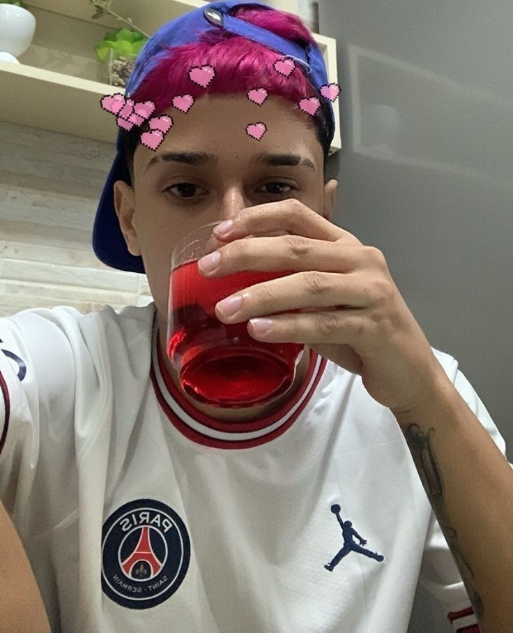 a woman with pink hair drinking from a glass in front of her face and wearing a headband