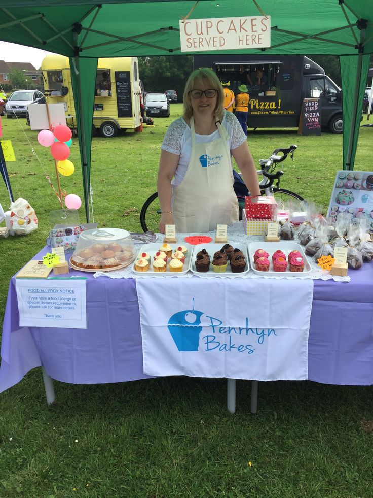 a woman standing in front of a table filled with cakes and cupcakes under a tent