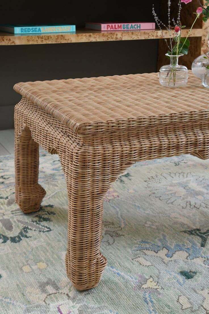 a wicker coffee table sitting on top of a rug next to a book shelf