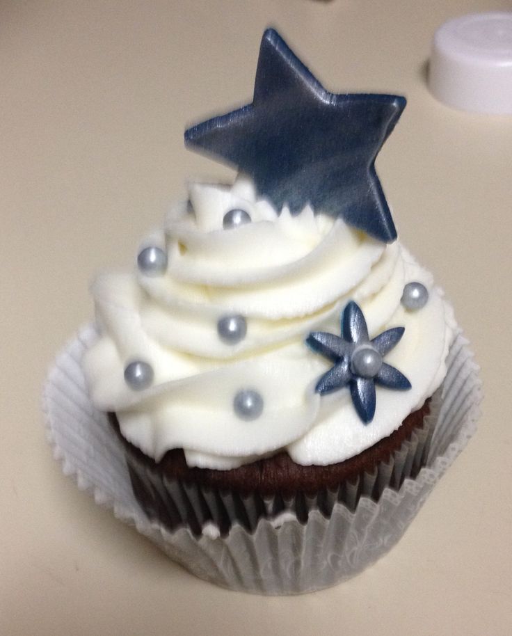 there is a cupcake with white frosting and blue stars on top, sitting on a table