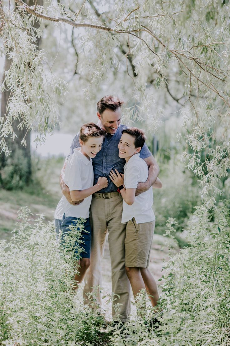 a man and two boys hugging each other while standing in tall grass under a tree