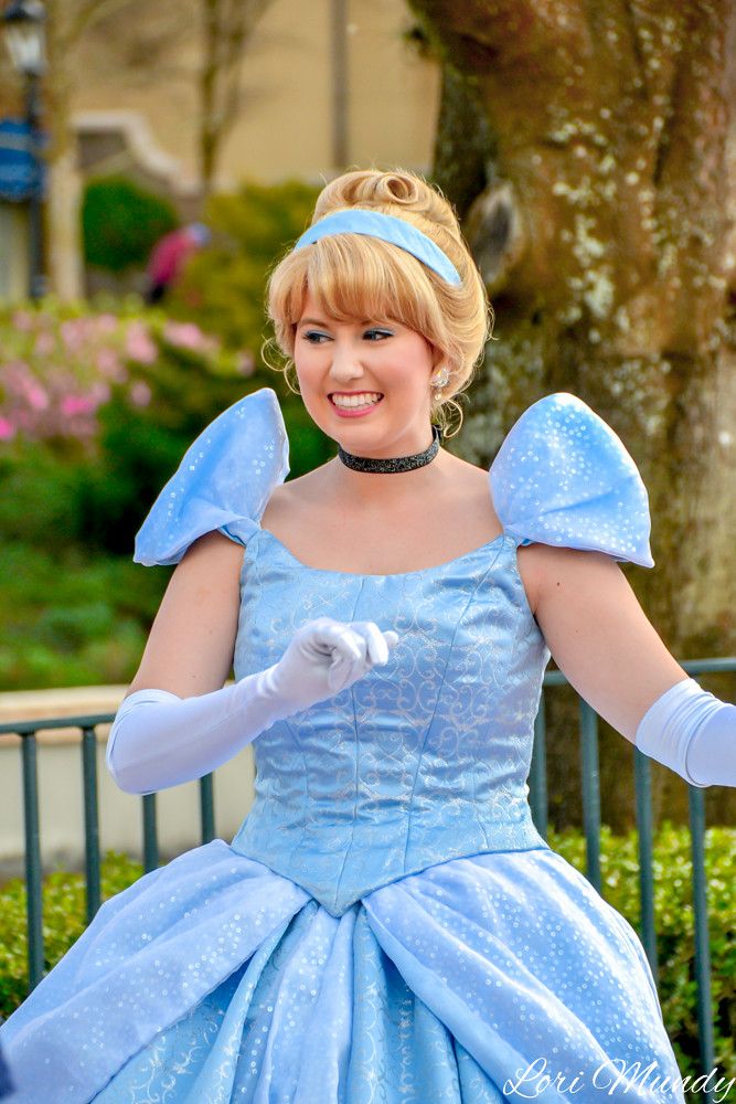 a woman in a blue dress and white gloves smiles at the camera while standing outside