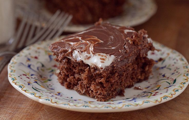 a piece of chocolate cake on a plate with a fork and glass of milk in the background