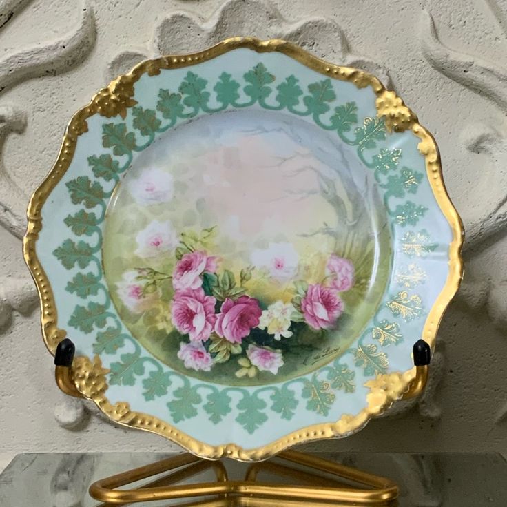 a plate with flowers painted on it is sitting on a stand in front of a wall