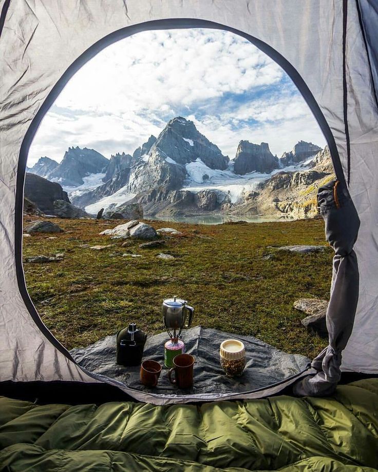 there is a tent in the field with mountains in the background and drinks on the table