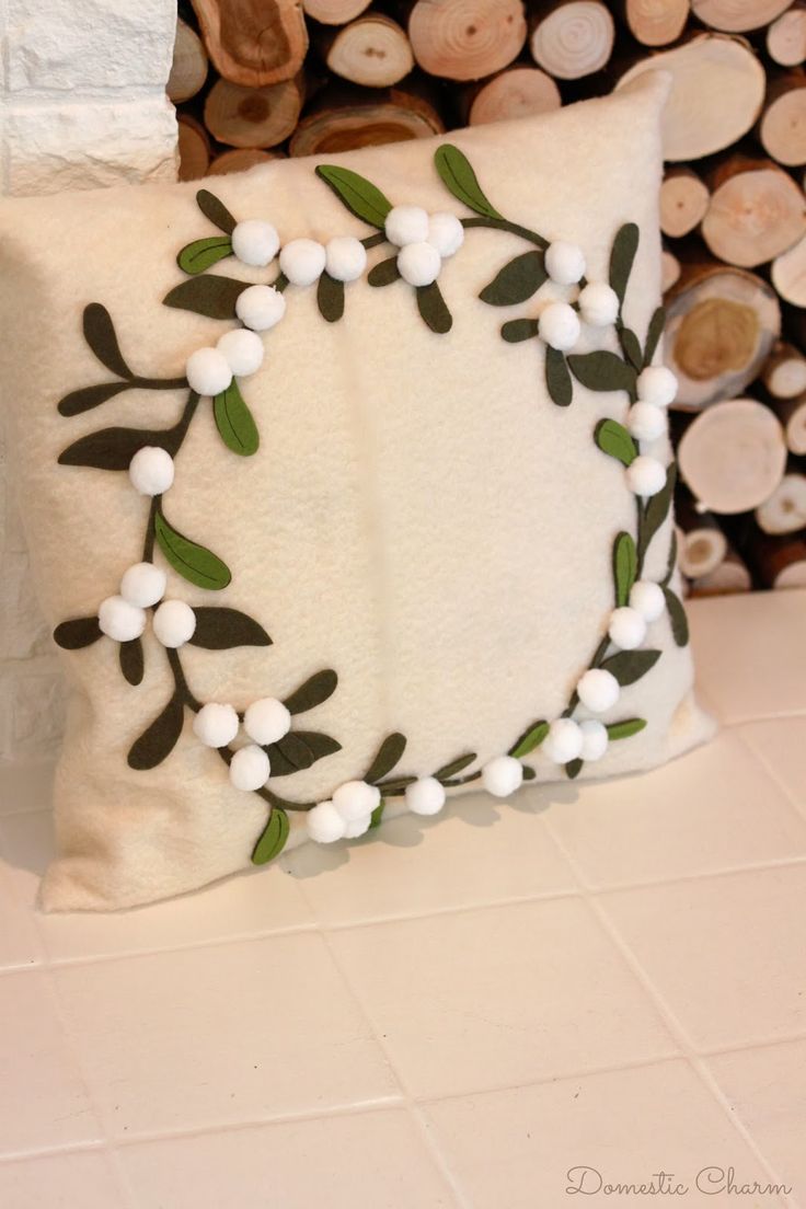 a white pillow with green leaves and berries on it sitting next to logs in the background