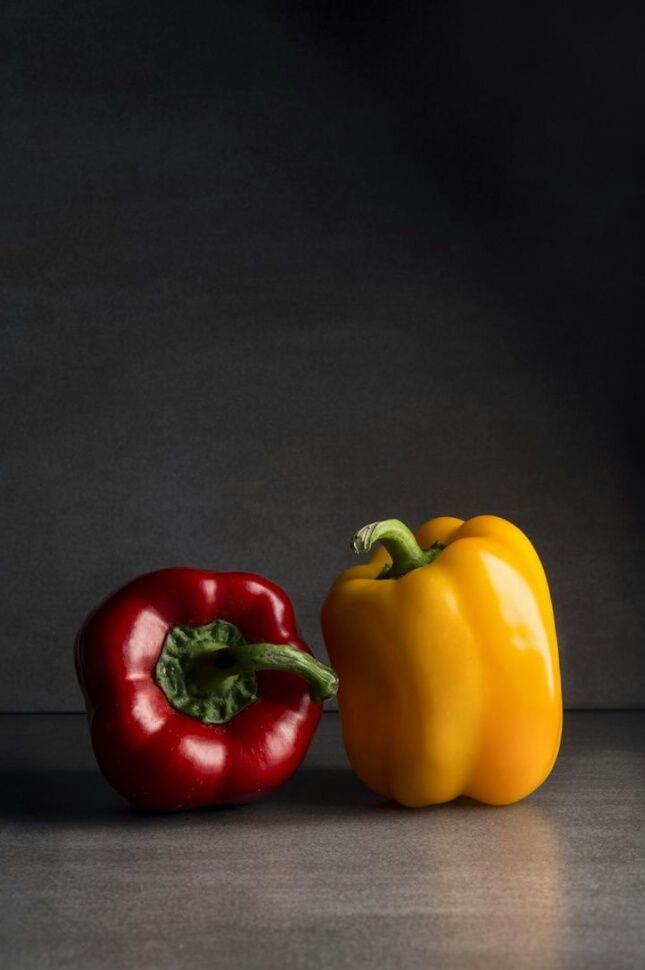 two peppers sitting next to each other on top of a metal surface with dark background