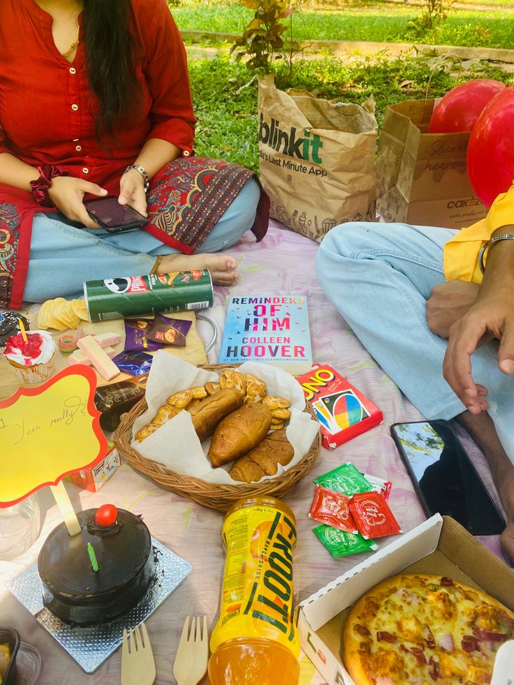 two people sitting at a picnic table with food and snacks on it, including pizza