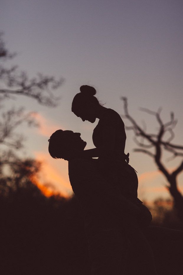 the silhouette of a man and woman in front of trees at sunset, with their arms around each other