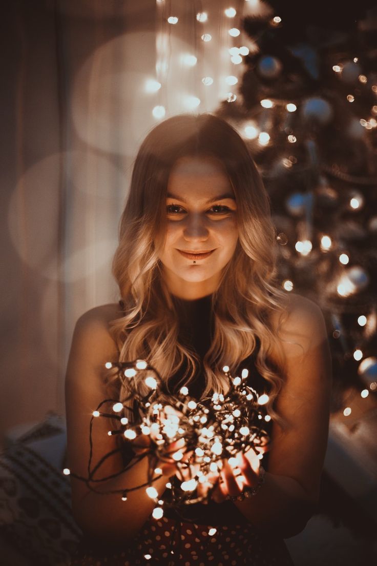 a woman holding a bouquet of flowers in front of a christmas tree with lights on it